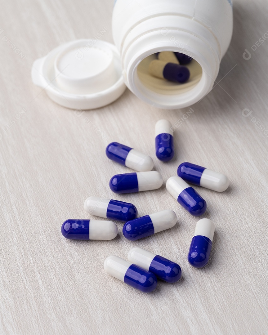 Imagem mostra cápsulas de medicamento azuis e brancas espalhadas e um frasco de medicamento aberto