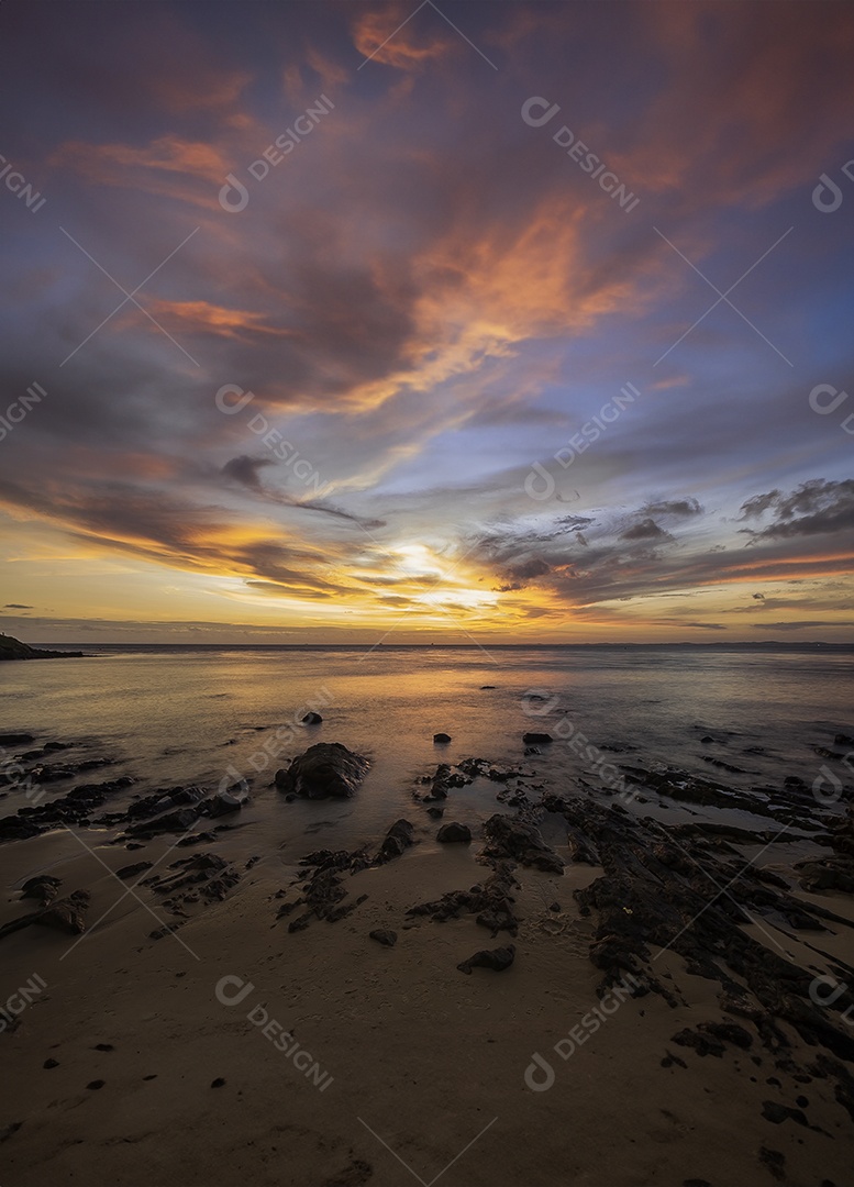 Pôr do sol vibrante sobre uma praia rochosa com nuvens e reflexos coloridos na água