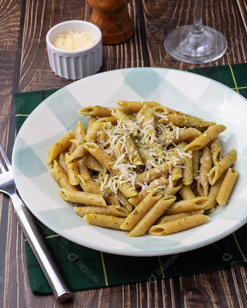 Prato na imagem é uma massa, especificamente penne, servida com molho pesto e queijo ralado
