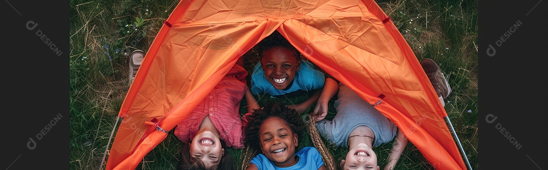 Foto panorâmica de crianças multiculturais felizes sorrindo enquanto estão deitadas perto do acampamento