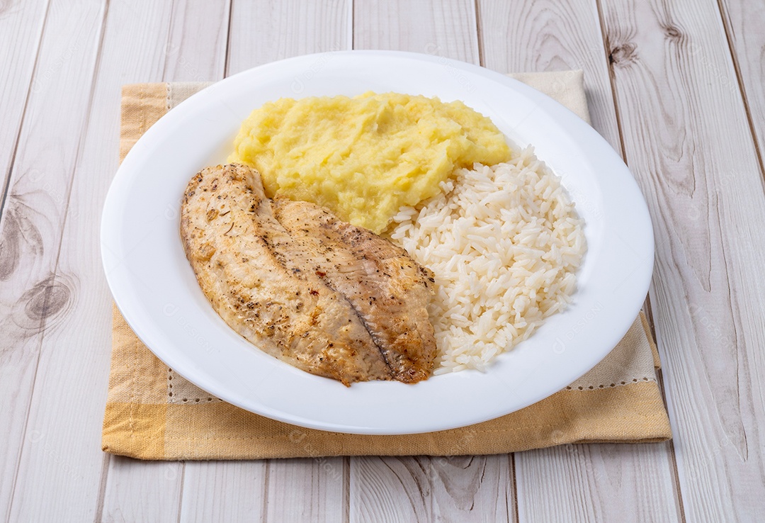 Prato de comida Filé de tilápia grelhado ou frito, com temperos visíveis na superfície. Arroz branco soltinho, servido ao lado do peixe. Purê de batata cremoso