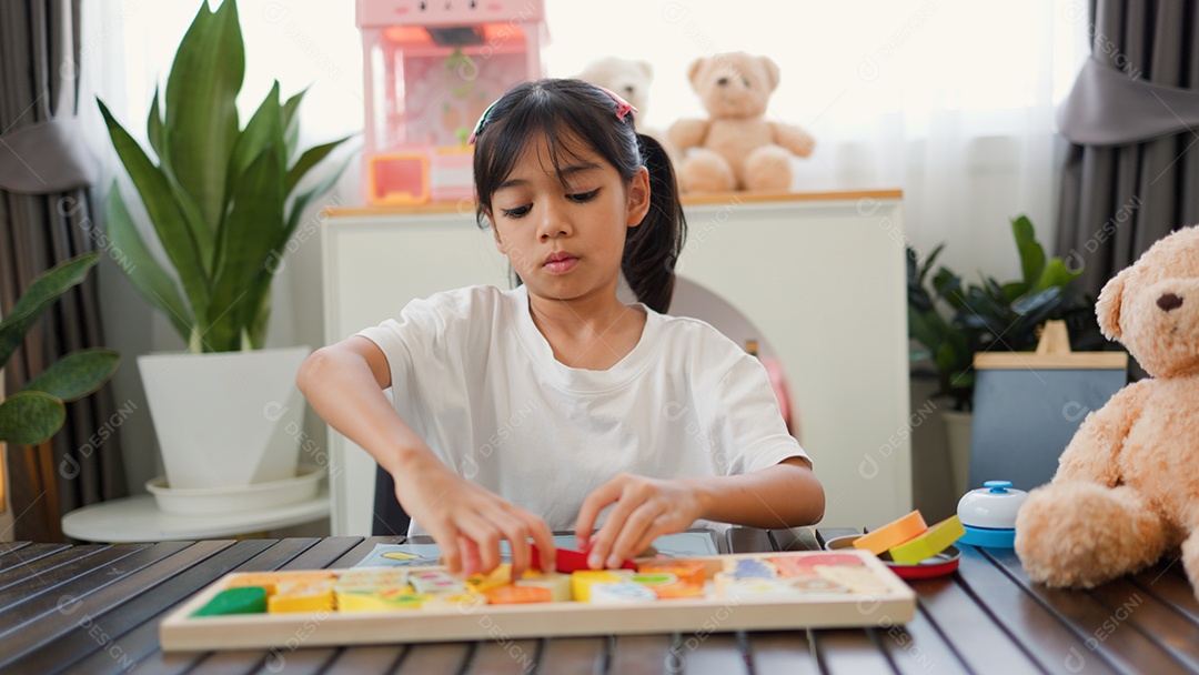 Menina asiática brincando com blocos de quebra-cabeça coloridos em casa