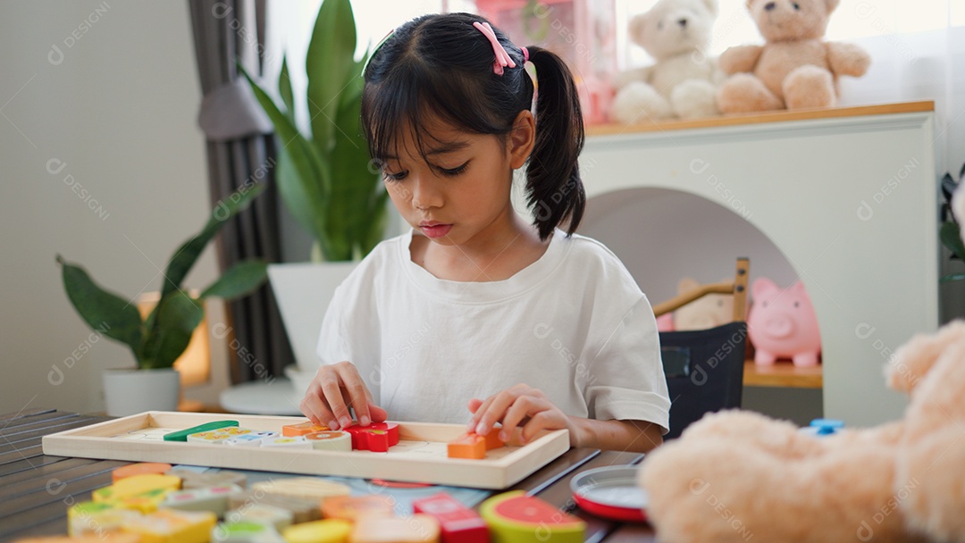 Menina asiática brincando com blocos de quebra-cabeça coloridos em casa