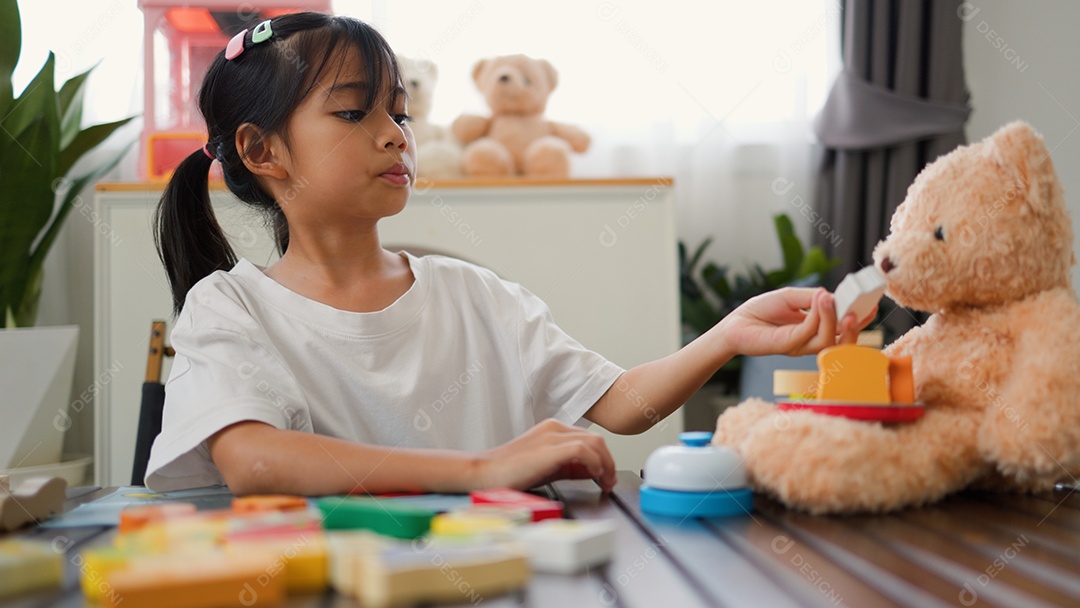 Menina asiática brincando com blocos de quebra-cabeça coloridos em casa
