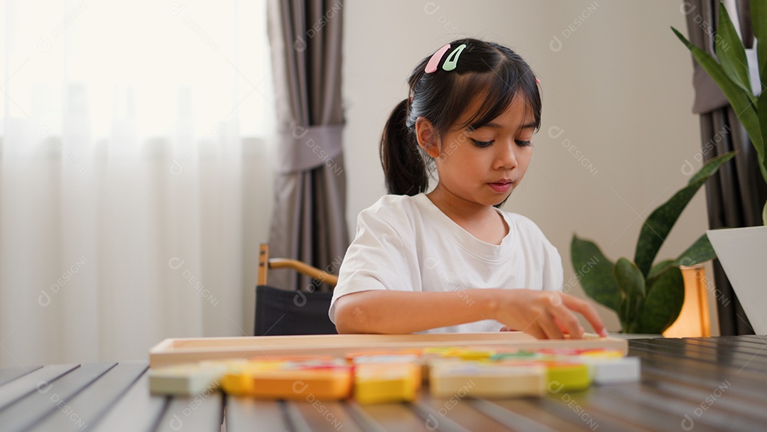 Menina asiática brincando com blocos de quebra-cabeça coloridos em casa