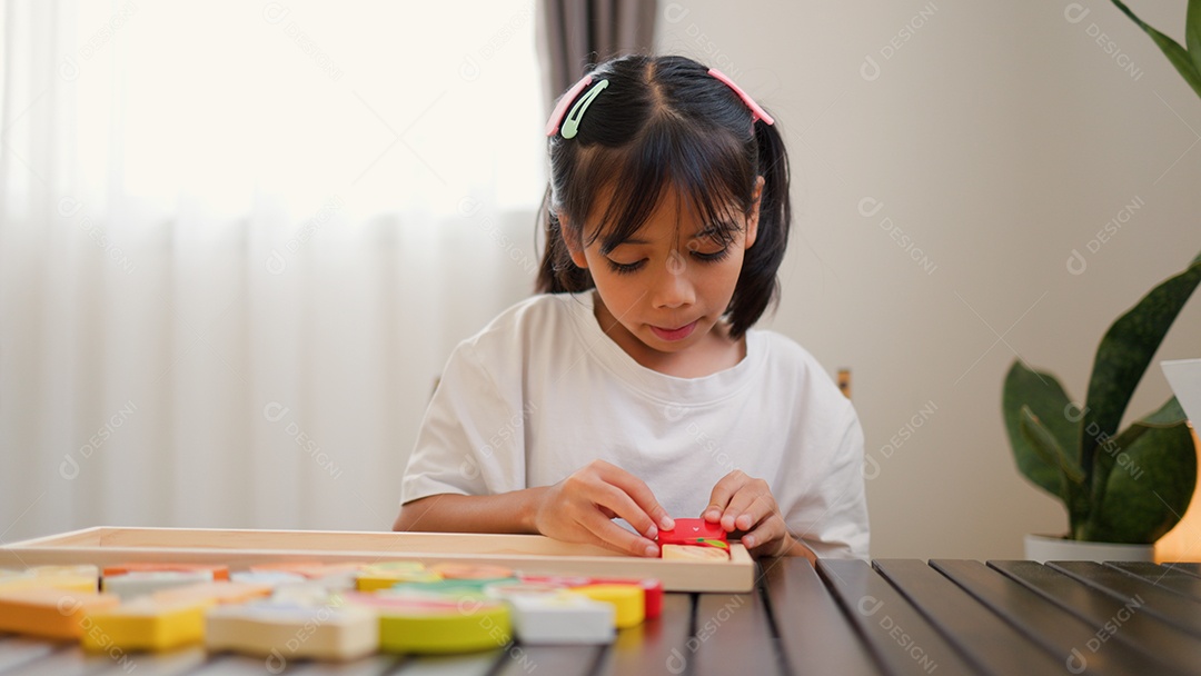 Menina asiática brincando com blocos de quebra-cabeça coloridos em casa
