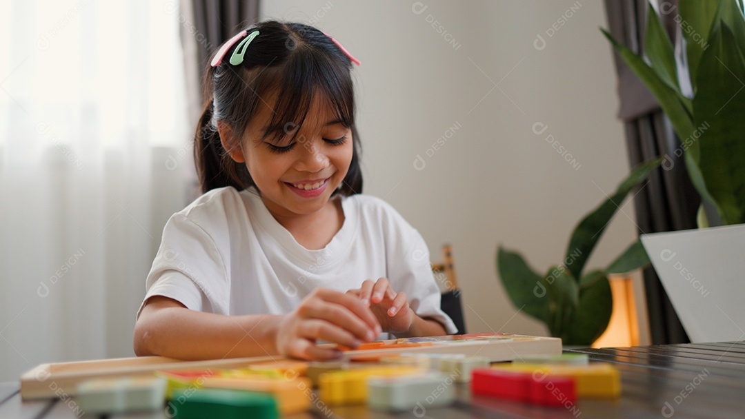 Menina asiática brincando com blocos de quebra-cabeça coloridos em casa