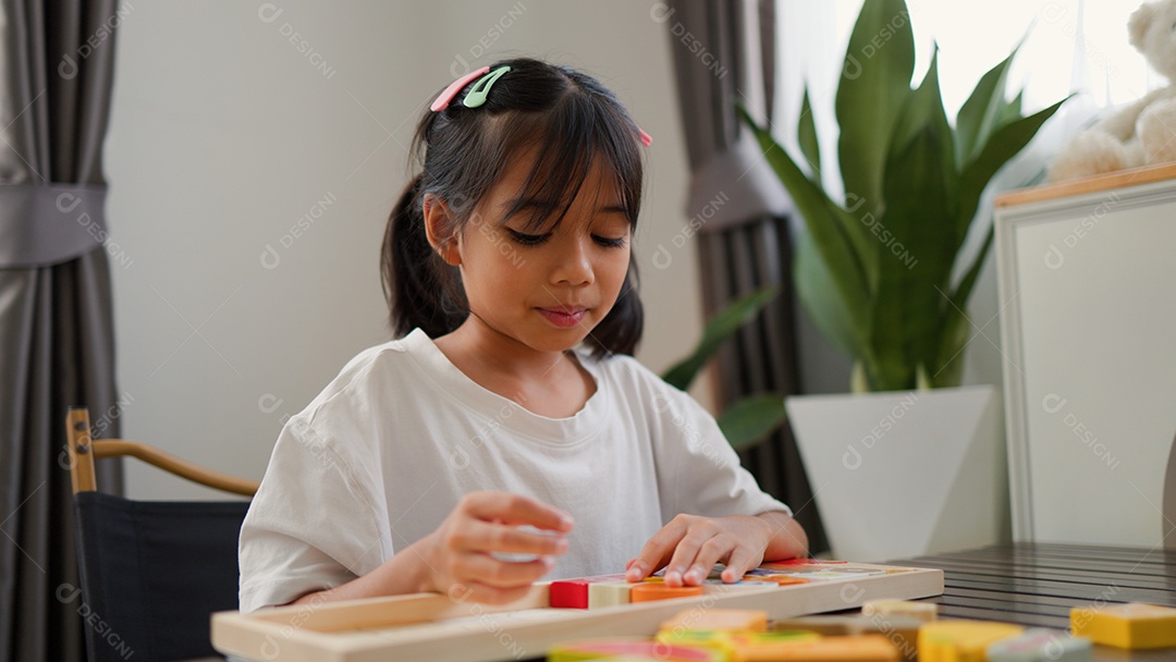 Menina asiática brincando com blocos de quebra-cabeça coloridos em casa