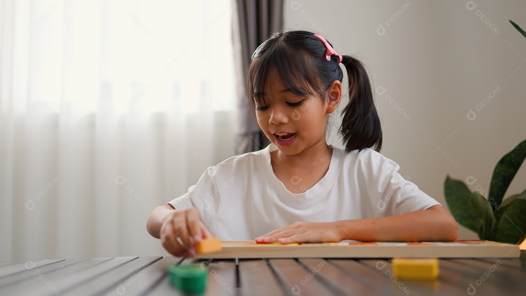 Menina asiática brincando com blocos de quebra-cabeça coloridos em casa