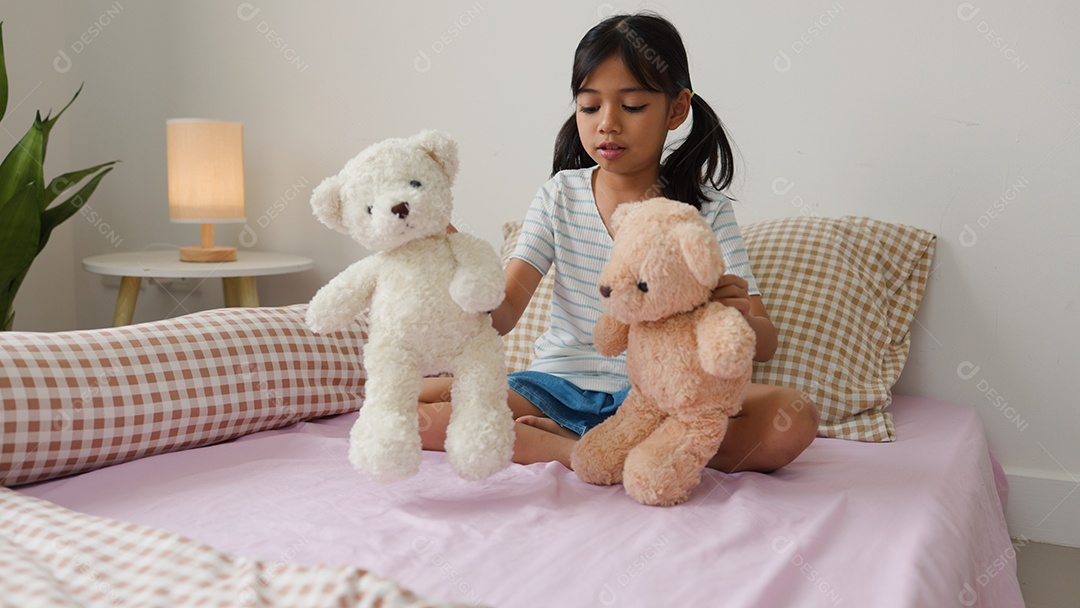 Linda garota asiática brincando com ursinhos de pelúcia na cama em um quarto aconchegante