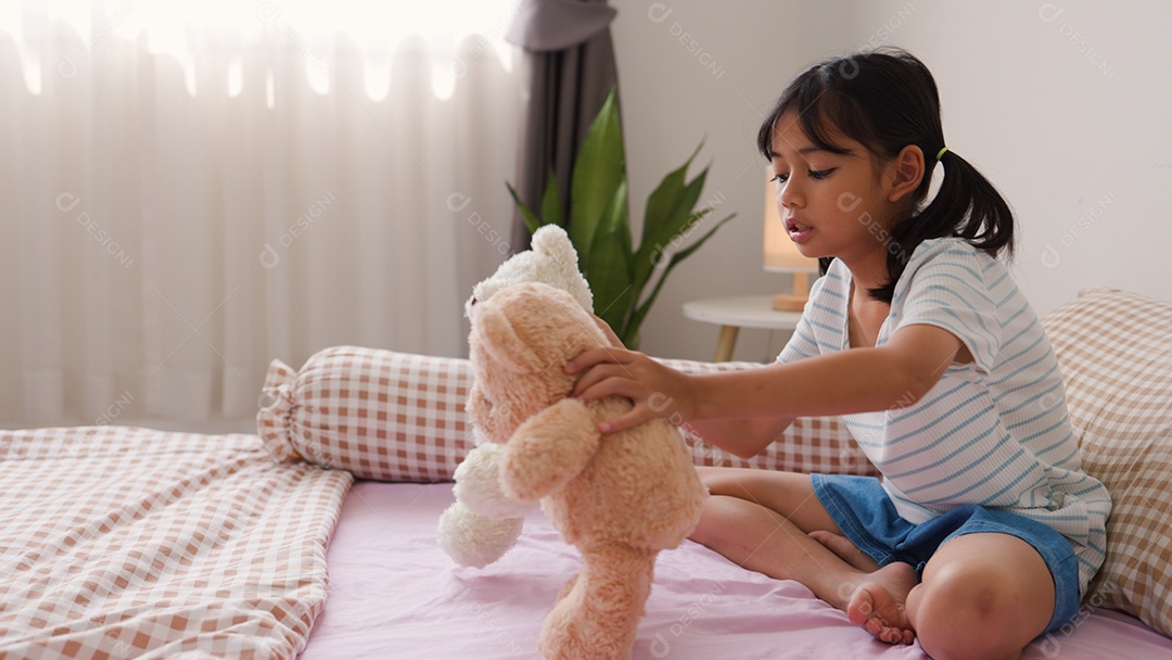 Linda garota asiática brincando com ursinhos de pelúcia na cama em um quarto aconchegante