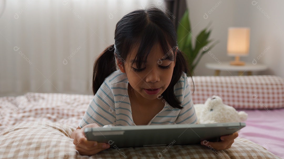 Garota asiática feliz deitada na cama usando tablet