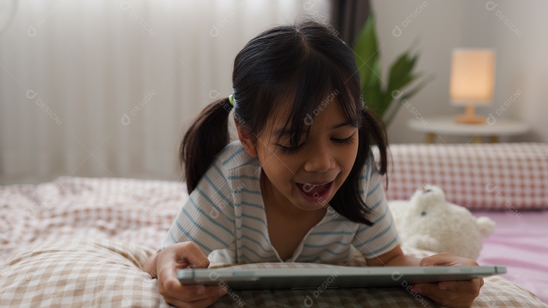 Garota asiática feliz deitada na cama usando tablet