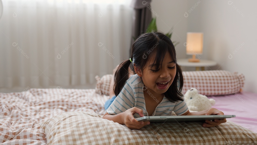 Garota asiática feliz deitada na cama usando tablet