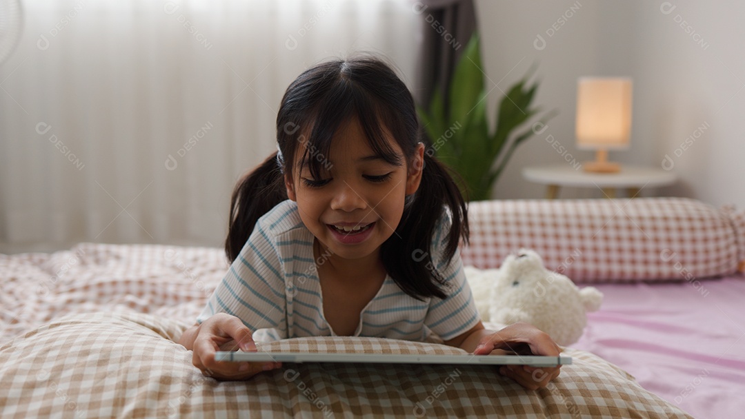 Garota asiática feliz deitada na cama usando tablet