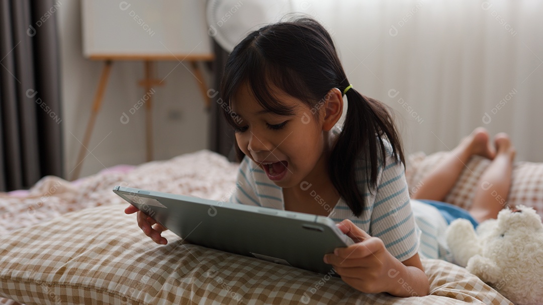 Garota asiática feliz deitada na cama usando tablet