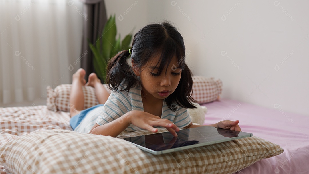 Garota asiática feliz deitada na cama usando tablet