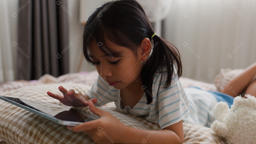 Garota asiática feliz deitada na cama usando tablet