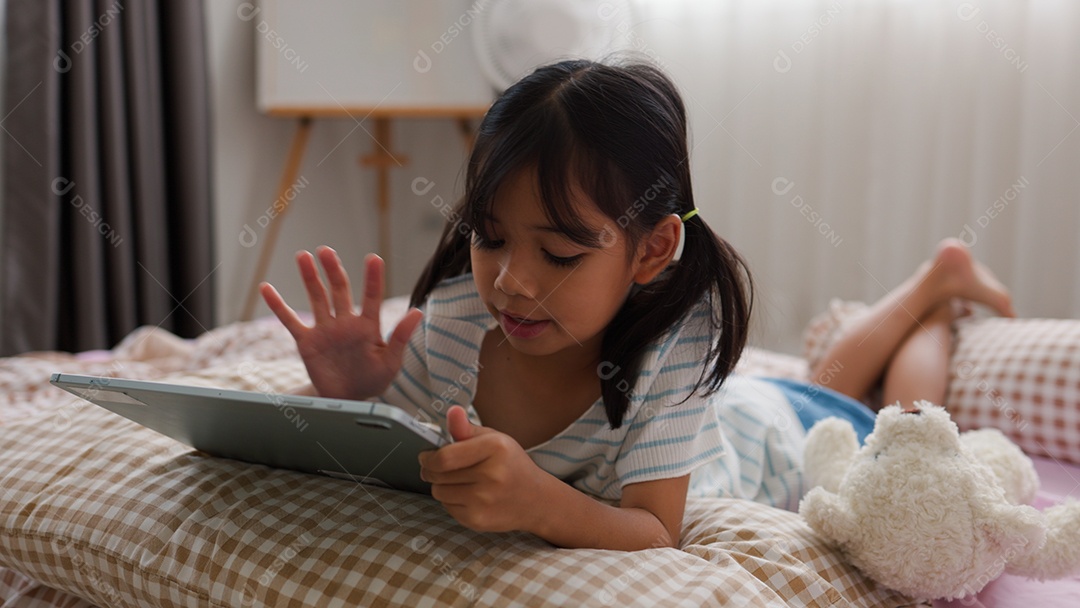 Garota asiática feliz deitada na cama usando tablet