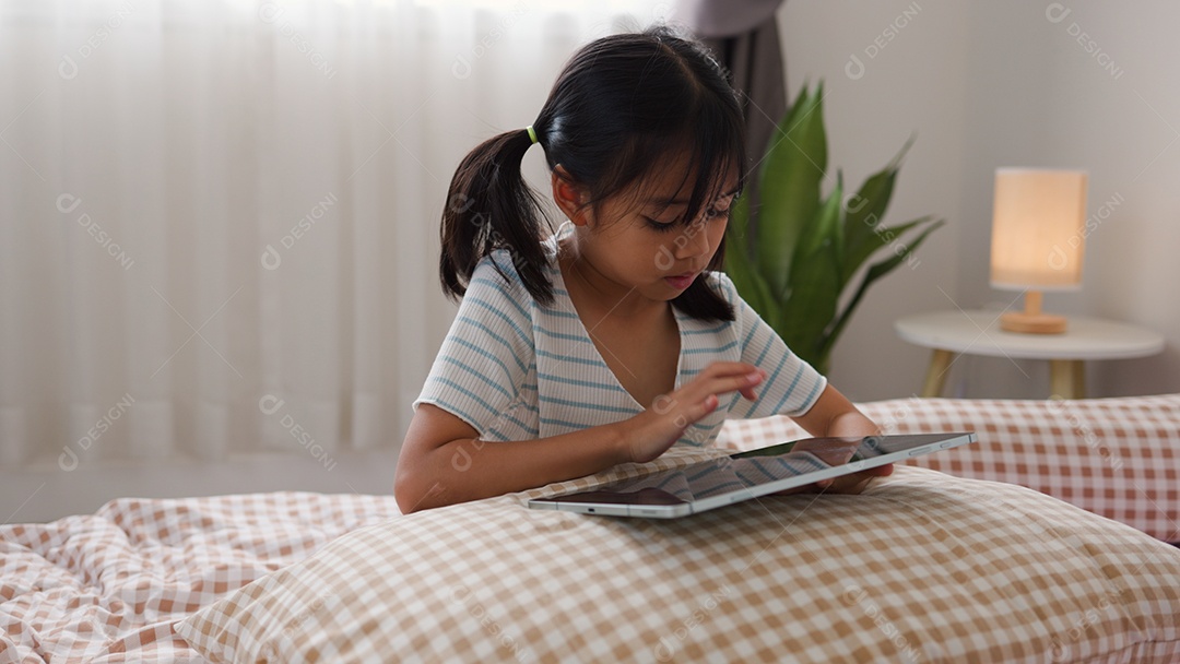 Garota asiática feliz deitada na cama usando tablet