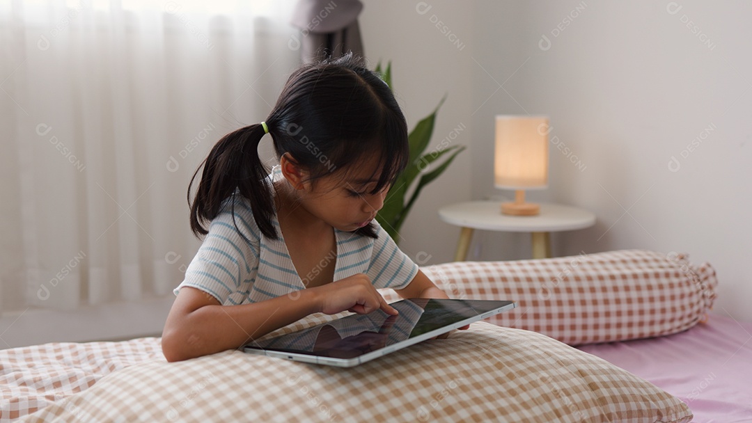 Garota asiática feliz deitada na cama usando tablet