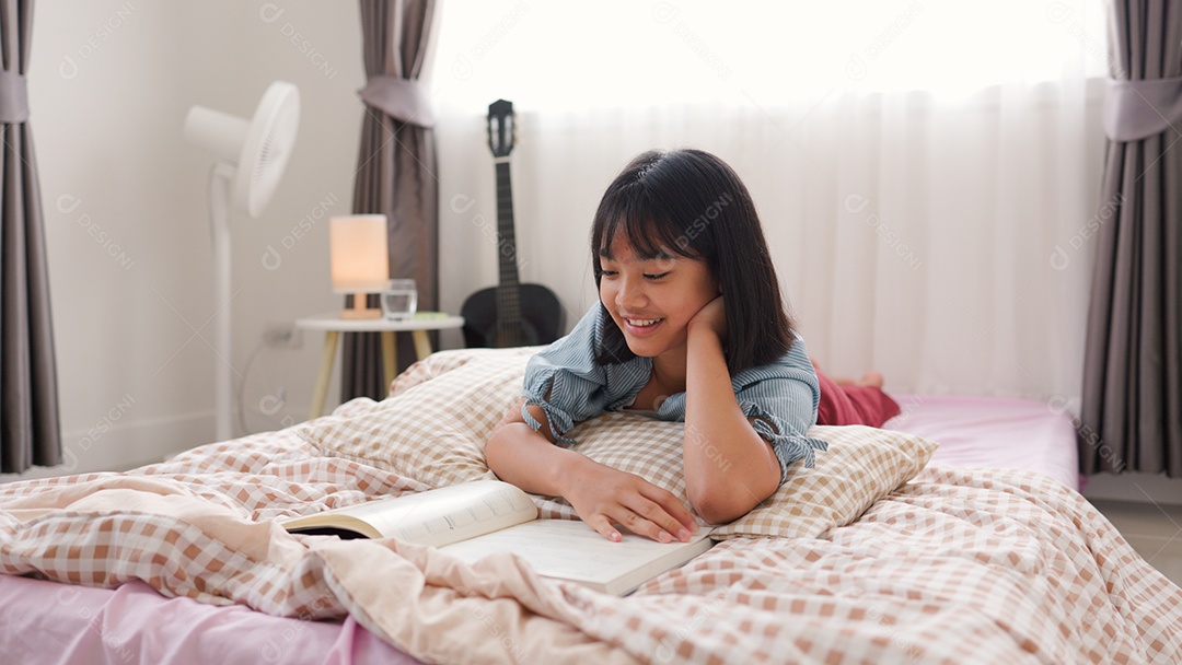 Menina asiática lendo um livro enquanto está sentada na cama em um quarto aconchegante