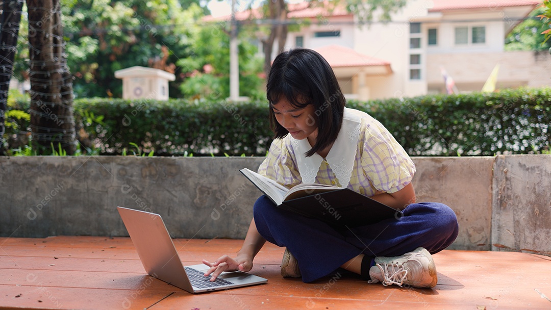 Adolescente asiática estudando ao ar livre usando um laptop e um livro