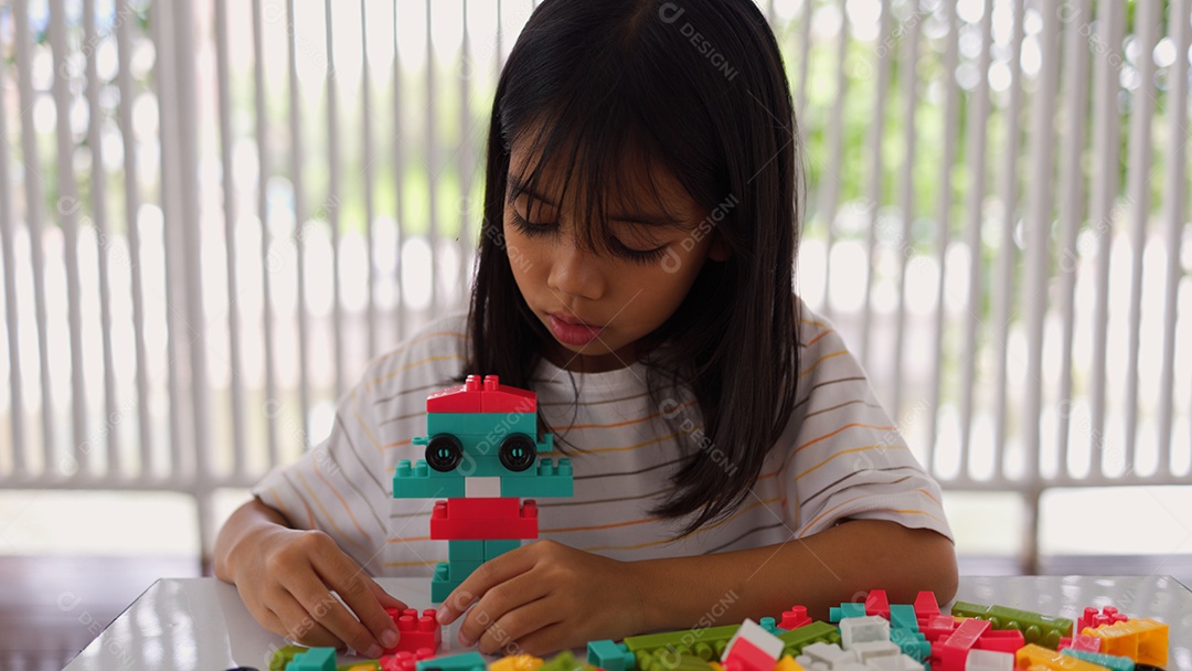 Menina asiática brincando com blocos de construção coloridos em casa