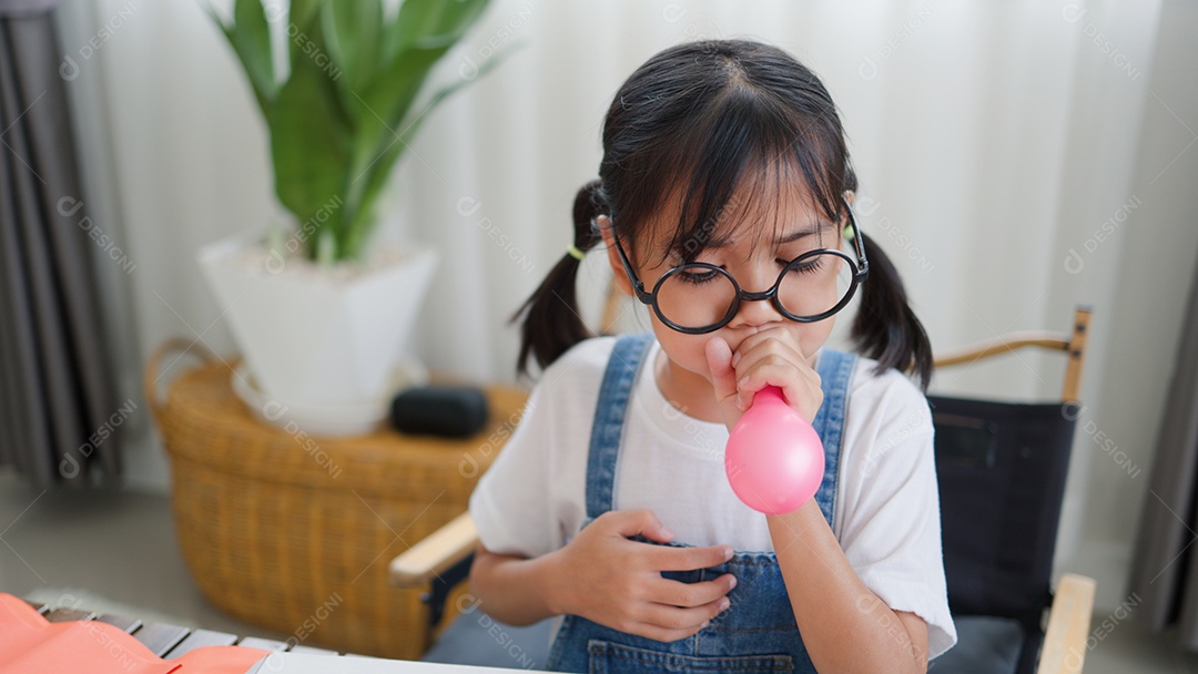 Menina asiática soprando um balão amarelo em casa