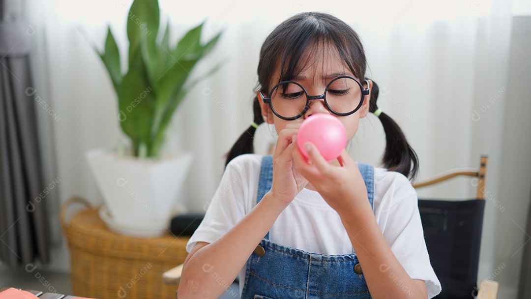 Menina asiática soprando um balão amarelo em casa