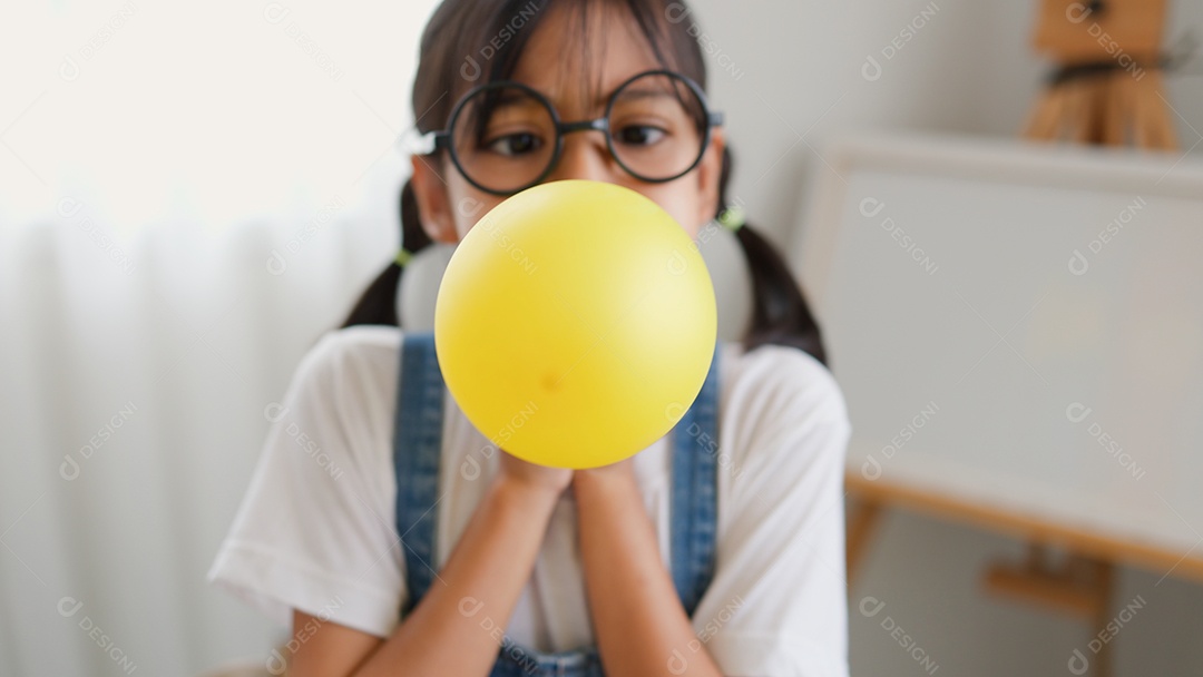 Menina asiática soprando um balão amarelo em casa