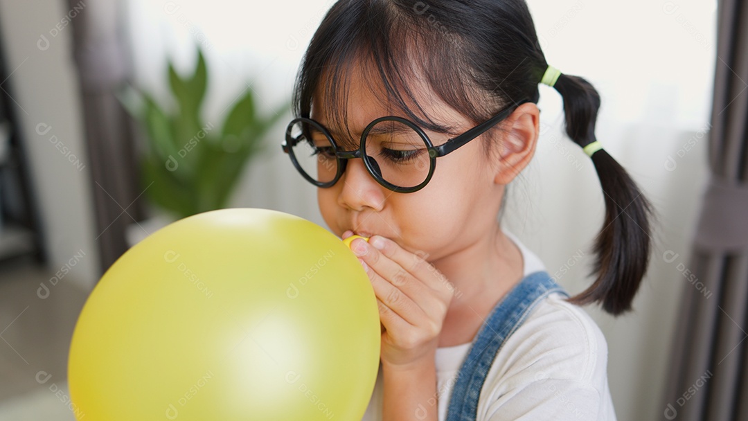 Menina asiática soprando um balão amarelo em casa