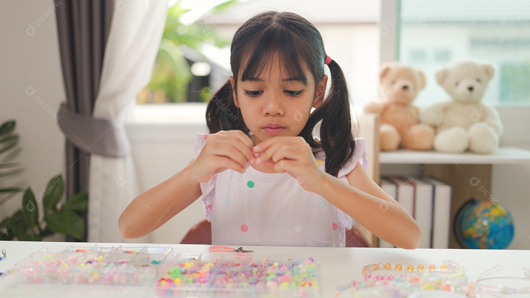 Garota asiática enfiando contas coloridas em casa