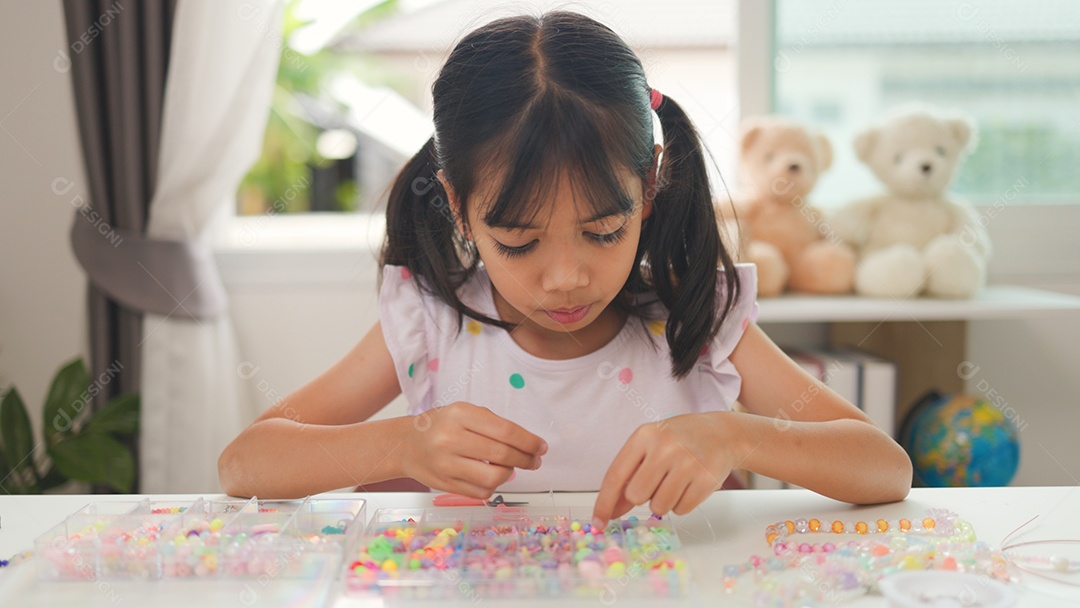 Garota asiática enfiando contas coloridas em casa