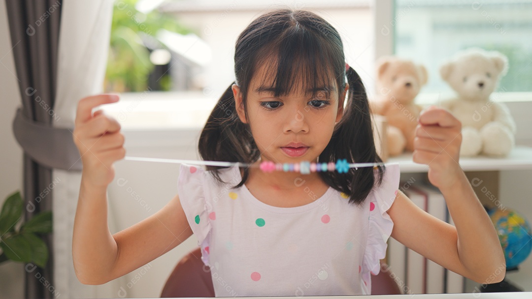 Garota asiática enfiando contas coloridas em casa