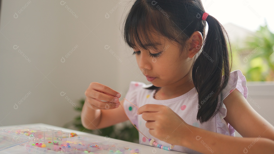 Garota asiática enfiando contas coloridas em casa