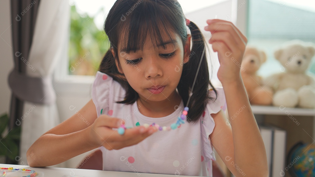 Garota asiática enfiando contas coloridas em casa