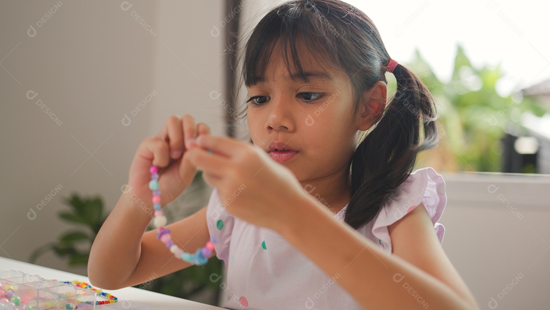 Garota asiática enfiando contas coloridas em casa