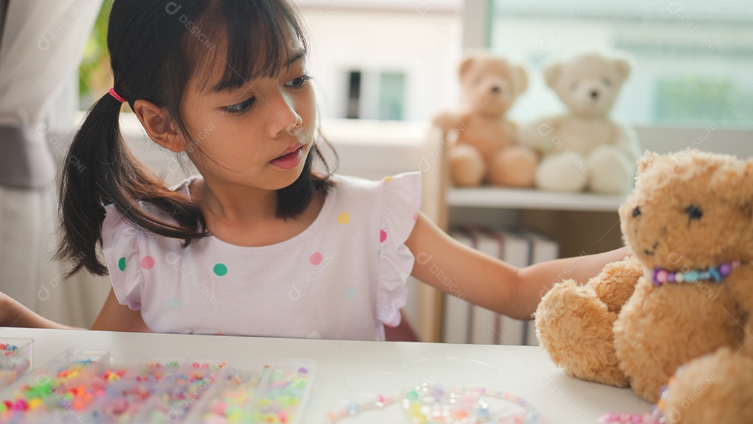 Garota asiática enfiando contas coloridas em casa