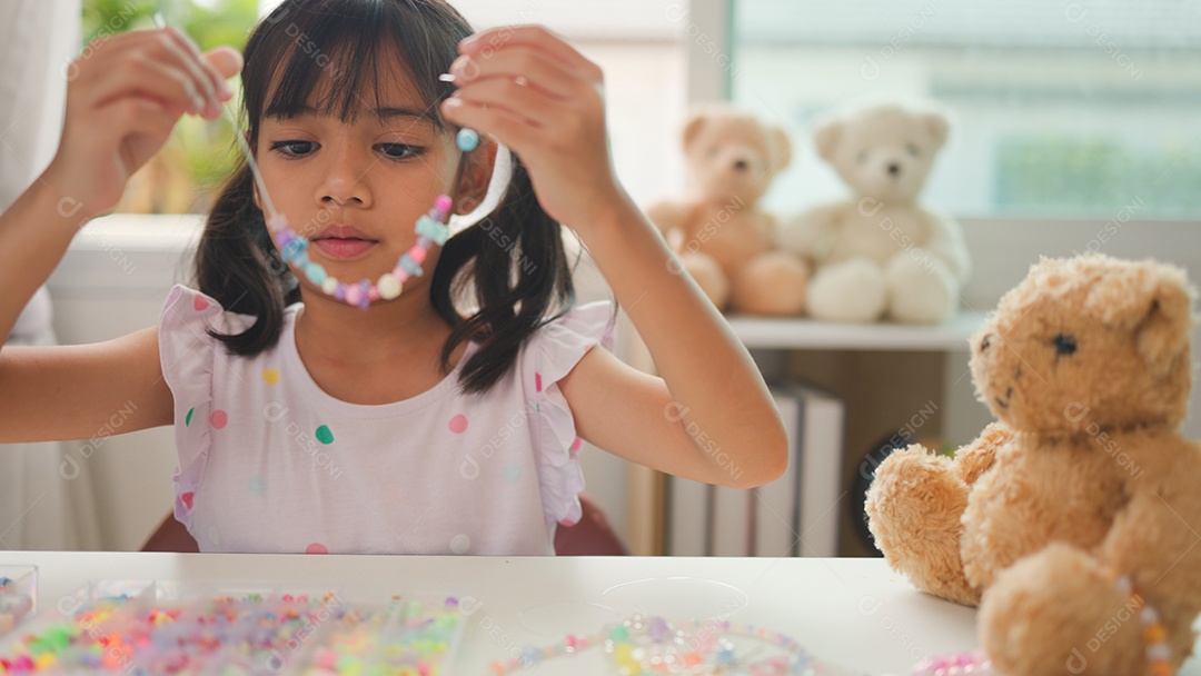 Garota asiática enfiando contas coloridas em casa