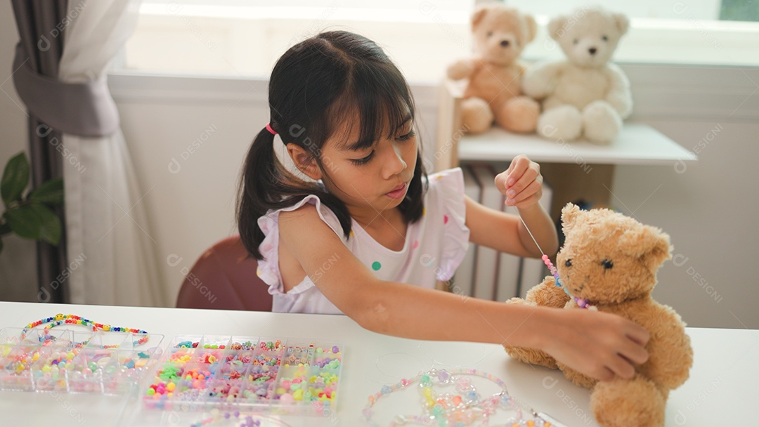 Garota asiática enfiando contas coloridas em casa