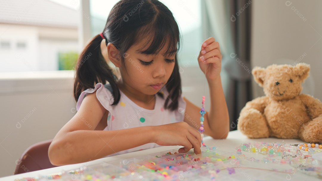 Garota asiática enfiando contas coloridas em casa