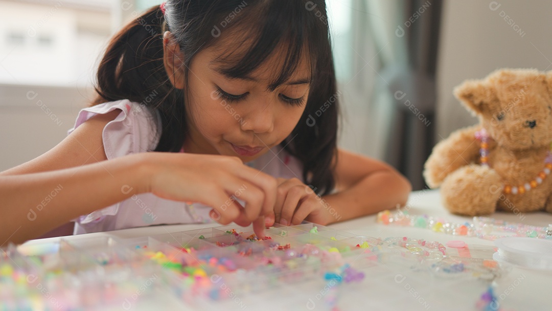 Garota asiática enfiando contas coloridas em casa