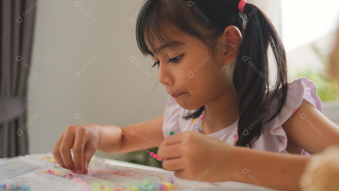 Garota asiática enfiando contas coloridas em casa