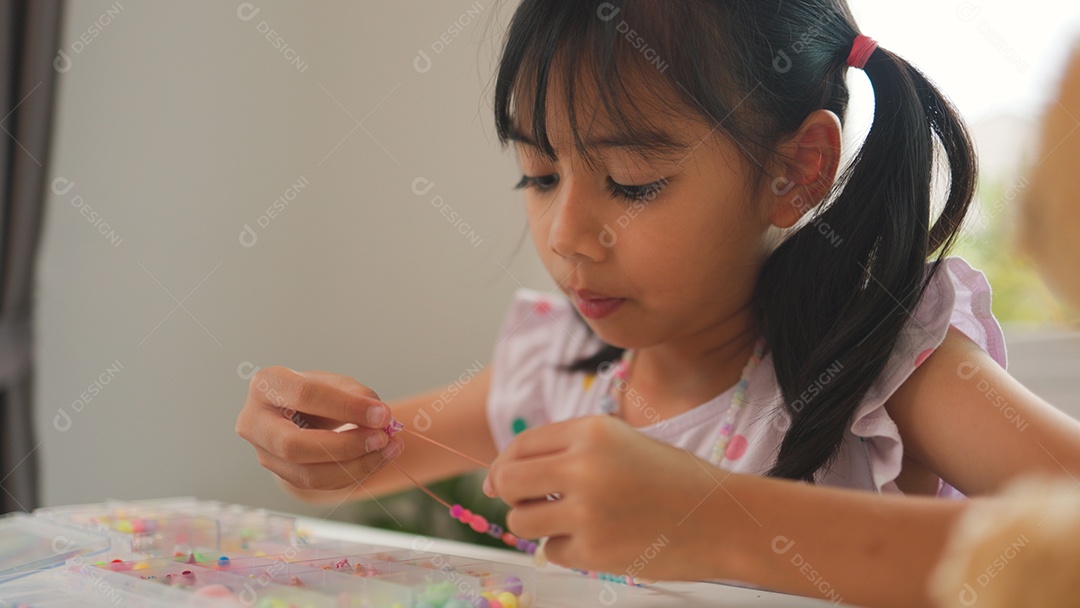 Garota asiática enfiando contas coloridas em casa