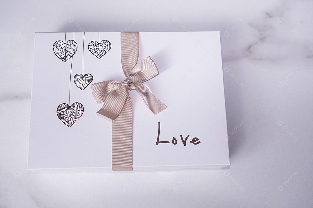 Uma caixa branca de chocolates decorada com corações um laço e a palavra amor
