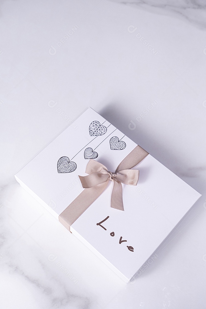 Uma caixa branca de chocolates decorada com corações um laço e a palavra amor