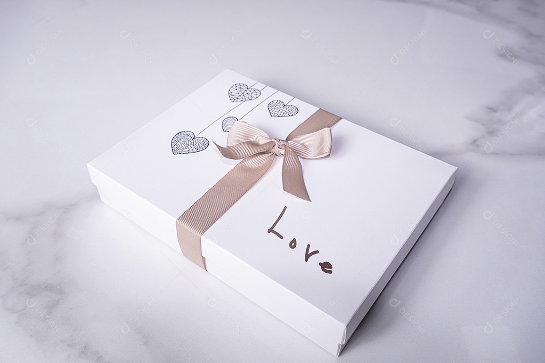 Uma caixa branca de chocolates decorada com corações um laço e a palavra amor