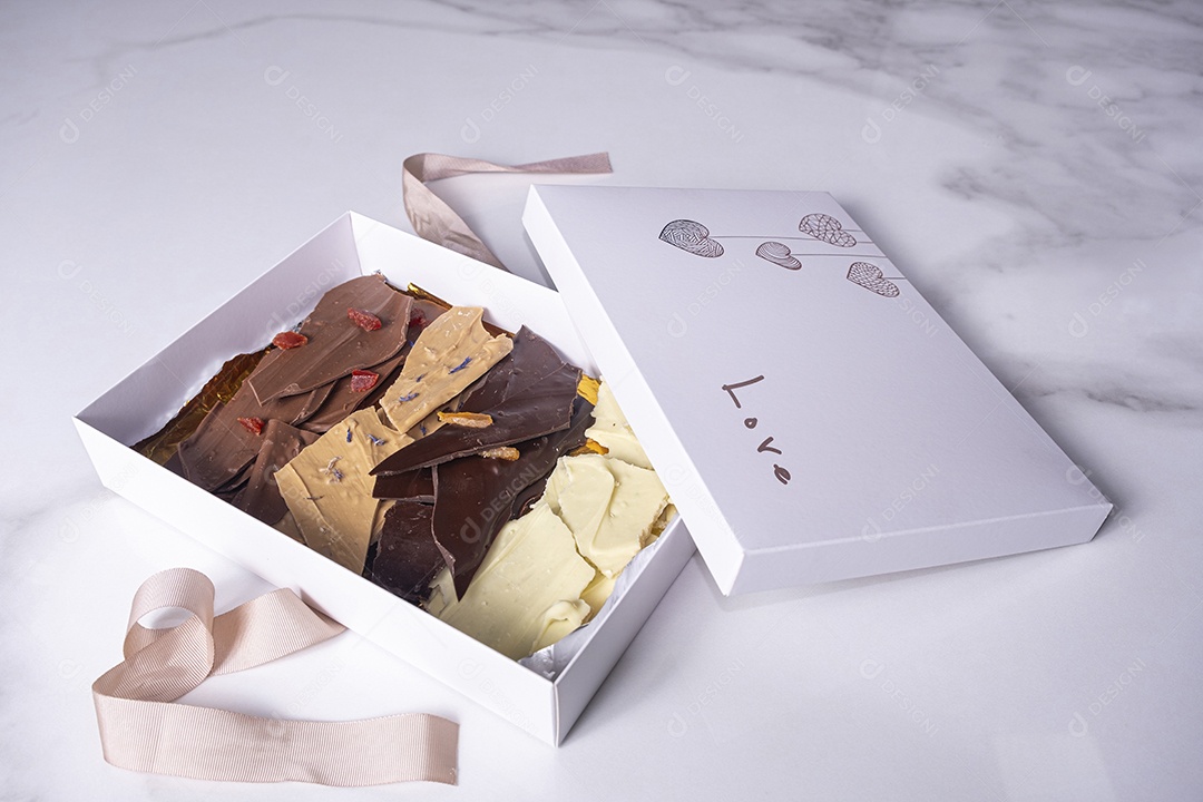 Uma caixa branca aberta com gotas de chocolate variadas