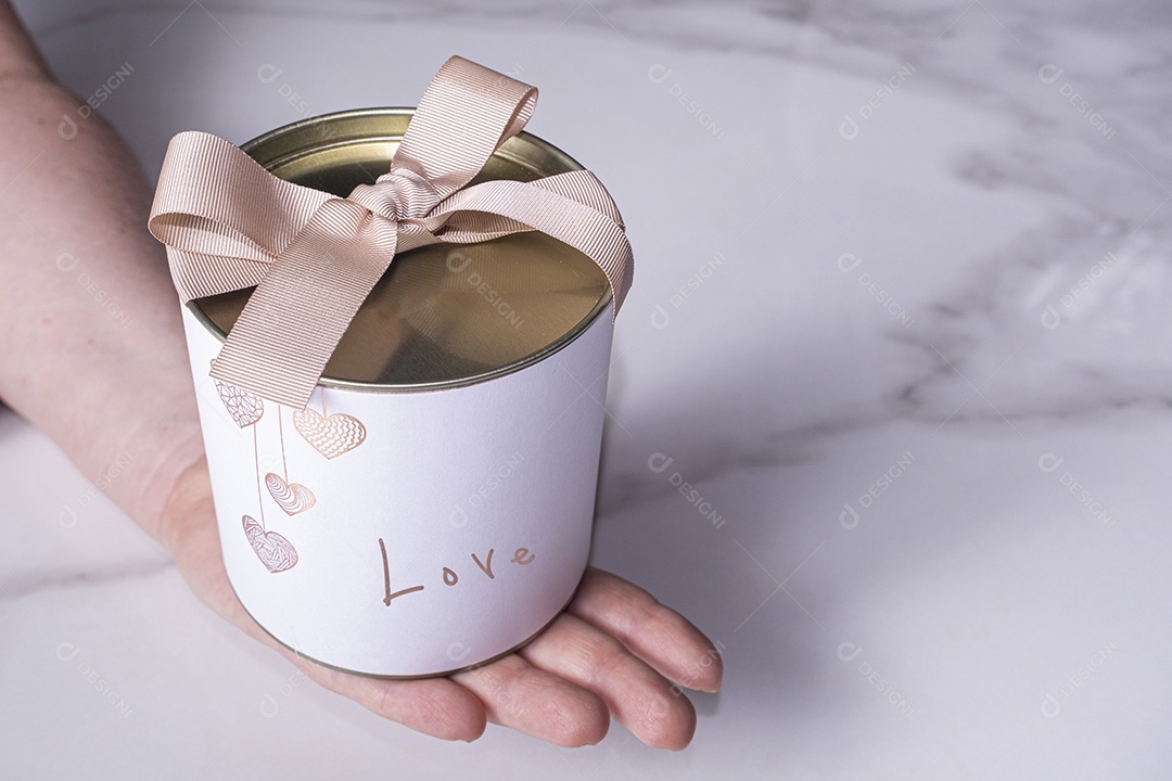 Uma caixa branca circular com uma tampa de metal sobre a mão de uma mulher